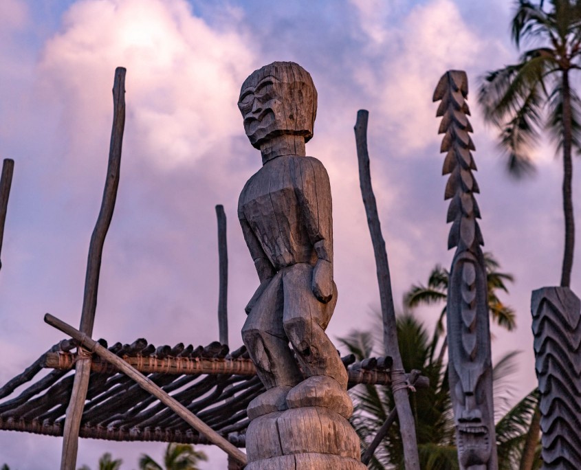 The setting sun lights the hand carved human figure atop the 'City of Refuge" near were Captain Cook landed